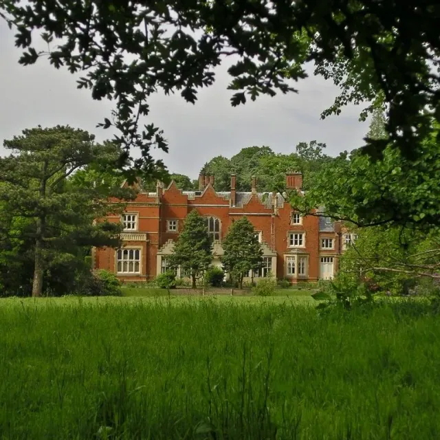 Abney Hall in Cheadle, a red-brick house with tall chimneys, seen across long grass under the trees